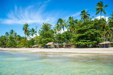 Bright sunny view of empty beach lined with rustic wooden beach shacks on the coast of a remote island in Bahia, Brazil