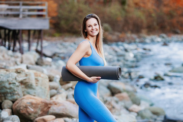 Portrait of a nice young girl pilates instructor standing against a background of blurred wildlife with a pad in her hands. Sports concept. Copyspace