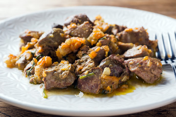 Stewed chicken liver with vegetables on a plate. Wooden background.
