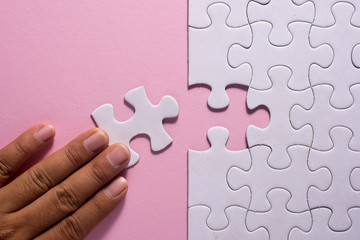 Close up of hand placing the last jigsaw puzzle piece on pink background. Business and team work concept.
