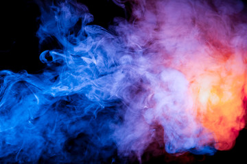 Multicolored smoke like cosmic dust of blue, red, magenta and fiery orange on a black background is...