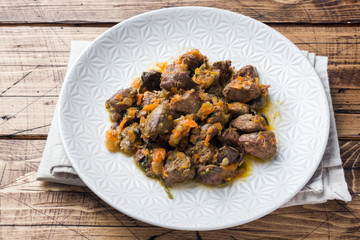 Stewed chicken liver with vegetables on a plate. Wooden background.