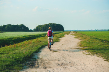 Obraz premium Young beautiful woman rides on a bicycle in the summertime on the green fields background