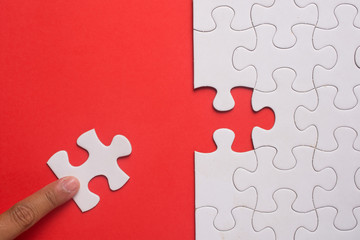 Close up of hand placing the last jigsaw puzzle piece on red background. Business and team work...