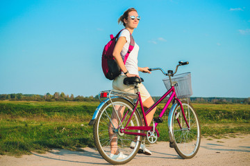 Fototapeta na wymiar Young beautiful woman standing with her pink bicycle closeup in the summertime on the green fields background