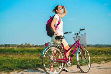 Young beautiful woman standing with her pink bicycle closeup in the summertime on the green fields background