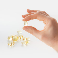 A girl's hand holds one transparent pill over a small handful of other transparent pills on a white isolated background
