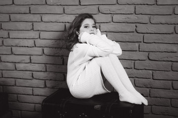 Little beautiful girl with brown hair in a white sweater. Studio. A princess poses for a photographer. Makeup and hairstyle