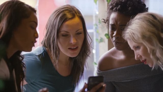 Female friends gathered around a cell phone in a coffee shop