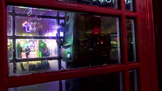 London old scratched red telephone booth night street illumination glass reflecion.