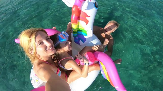 Happy family with little girl taking selfie in the sea seating on the inflatable unicorn