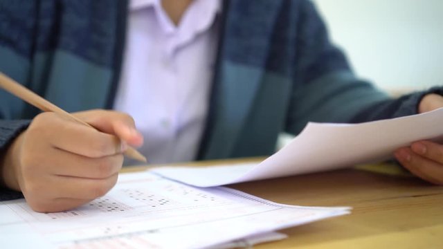 School / university Students hands taking exams, writing examination room with holding pencil on optical form answers paper sheet on desk doing final test in classroom. Education assessment Concept