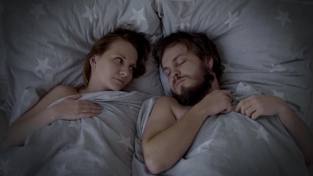 Man Snoring in Bed, Woman cannot sleep. Husband snoring, his Wife is Waking up and closing her ears. Spouses are Sleeping in bedroom at Night. - Powered by Adobe