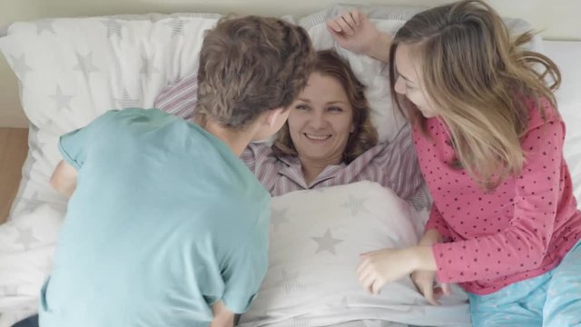 Mothers Day - Children surprise their Mum with presents in bed. Happy Family - beautiful Mother with her Son and Daughter. Girl and boy congratulates mom and gives her postcard.
