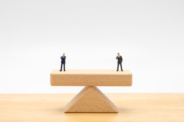 Miniature people businessmen Standing on wooden beams standing on both sides, weighing the importance of business concepts, maintaining benefits Conflict resolution