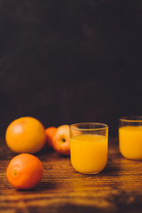healthy fruit including oranges grapefruits and apples scattered on wooden table and with juice glasses