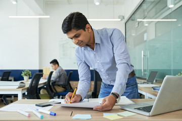 Smiling Indian man enjoying working as UI designer in big company