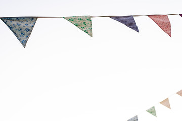Pennants with blue sky background and pale colors hanging on a rope crossing the image during an outdoor event, space for text.