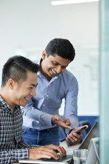 Laughing Indian businessman showing colleague something funny on smartphone screen