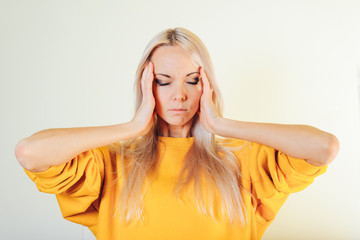 Fototapeta premium Portrait of an attractive blonde girl holding her hands on her head. The concept of headache, migraine.