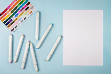 Markers for drawing and a white sheet of paper on a blue background.
