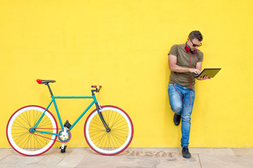 Front view of a young trendy man with a fixed bike wearing casual clothes while using a laptop...