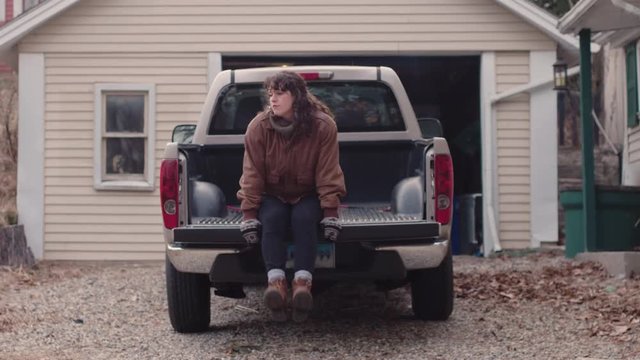 Young attractive woman dangles legs off pickup truck while thinking reflectively