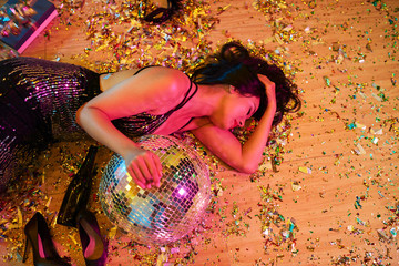 Drunk young woman lying on floor covered with confetti after partying all night long