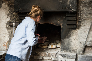 Young woman baking loaves of bread in an outdoor brick oven, Tuscany, Italy.