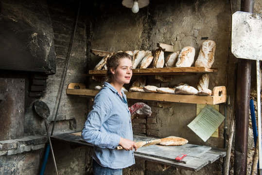 Young woman baking loaves of bread in an outdoor brick oven, Tuscany, Italy.