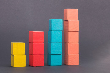 Obraz premium Toy wooden blocks as financial graph. Graph with four 4 steps. Growing chart. Infographic diagram, chart over grey or black or dark background. Multi-colored wooden blocks.