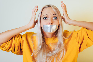 Portrait close-up of a girl with taped mouth holding hands on her head from what he saw terrible....
