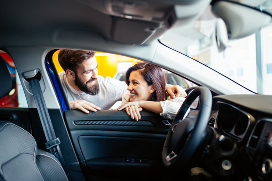 Beautiful Young Couple At Car Showroom Choosing A New Car To Buy.