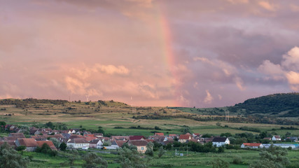 Obraz premium Scenic view of a rainbow over a Romanian village after summer rain, at sunset