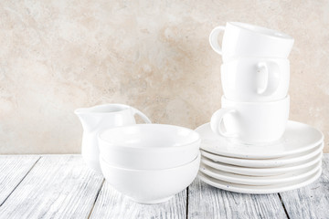 Assortment stack clean empty new white kitchen utensils, plates, bowls, cups mugs. On a white concrete background