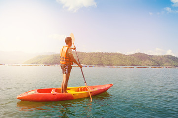 Man rowing with a paddle on the stand up on kayak with mountain landscape view