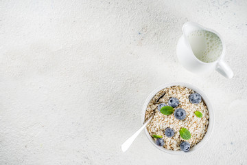 Healthy cereal and milk breakfast concept, dry oats in small bowl, with milk and fresh blueberry,...
