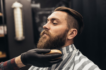 Hipster young good looking man visiting barber shop. Trendy and stylish beard styling and cut.