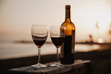 Bottle with red wine and glasses on the wooden, behind sunset