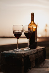 Bottle with red wine and glasses on the wooden, behind sunset
