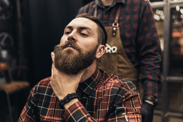 Hipster young good looking man visiting barber shop. Trendy and stylish beard styling and cut.