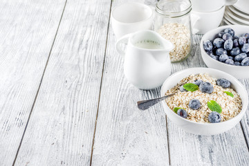 Healthy cereal and milk breakfast concept, dry oats in small bowl, with milk and fresh blueberry,...