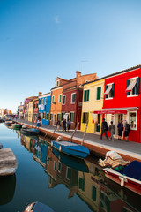 Fototapeta na wymiar Burano island picturesque street with small colorful houses, smal water canal with beautiful reflections and boats, Venice Italy 