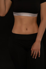 Slim and sexy stomach of woman on black background; sporty female  girl showing  her perfect body.