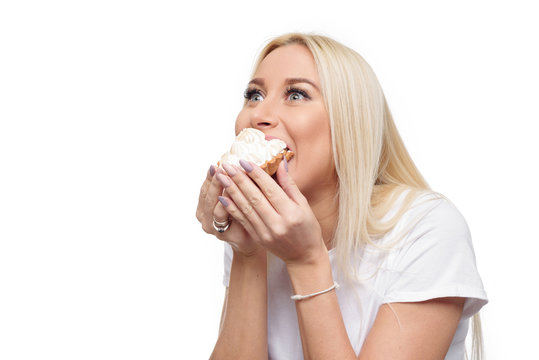 Diet. Dieting concept. Image of beautiful blond  woman in white clothe isolated over white background holding and eating cake with  pleasure 