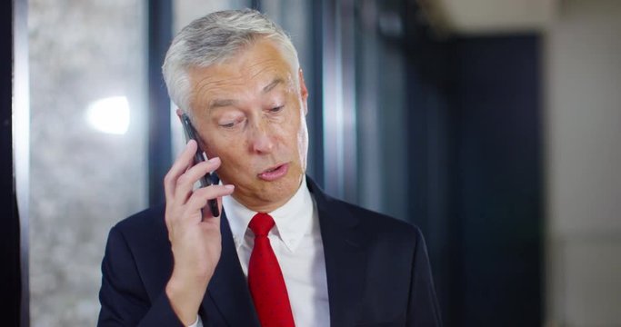 4K Attractive grey haired businessman talking sternly to someone over the phone