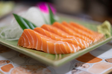 Close up of Salmon raw sashimi on green Japanese traditional dish on the table.