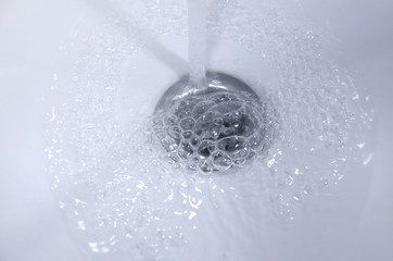 Naklejka na ściany i meble Transparent water flows into the sink drain. Image.
