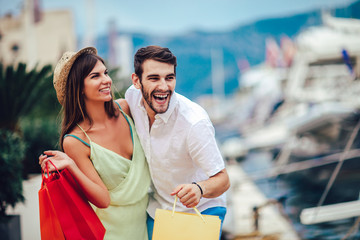 Happy young couple with shopping bags walking by the harbor of a touristic sea resort with boats on background