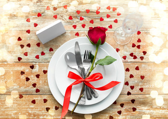 valentines day, table setting and romantic dinner concept - close up of red rose flower on set of dishes with cutlery, red rose, hearts and blank place card on wooden background